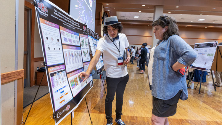 A student shows their poster presentation to a visitor at Create@state